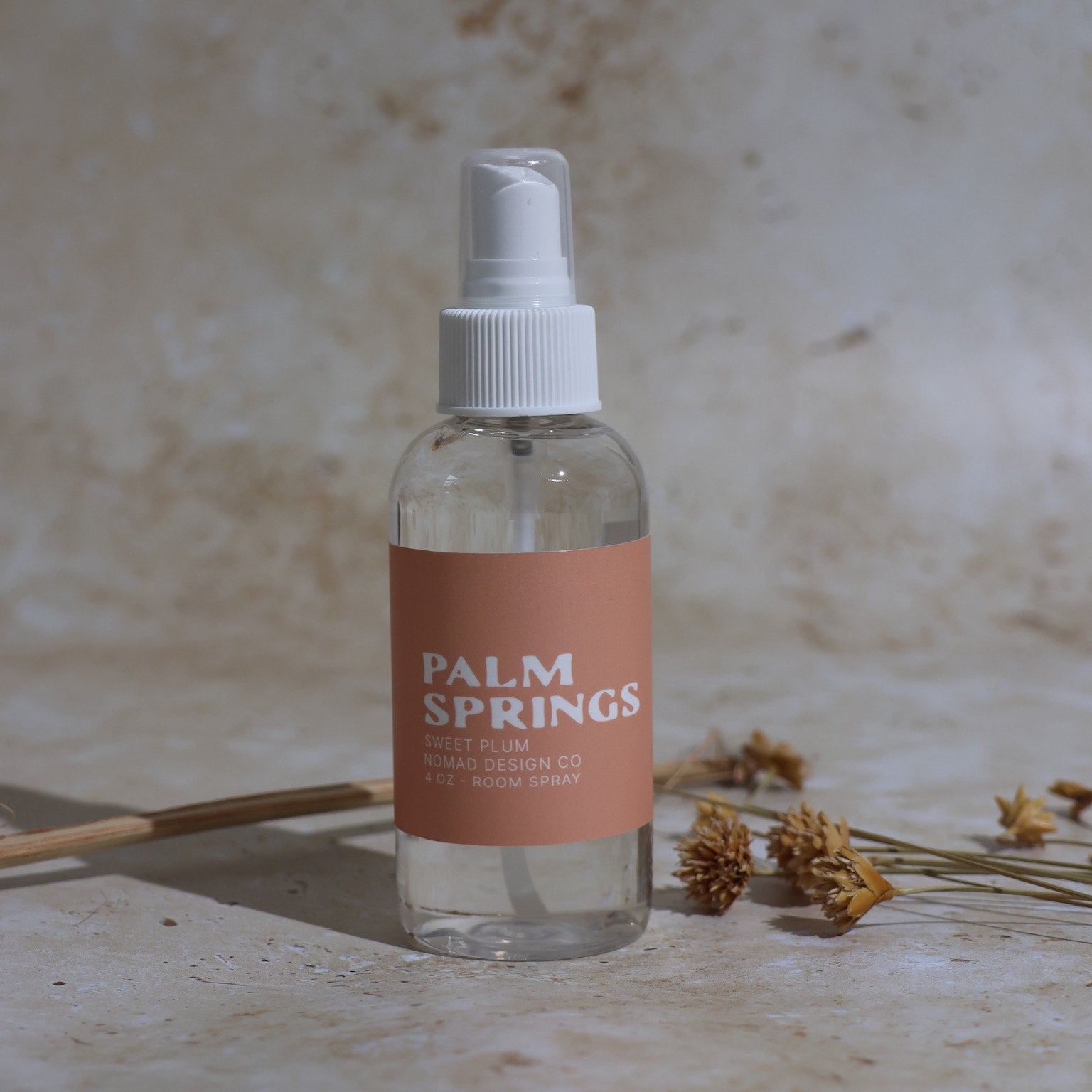Clear spray bottle with a 'Palm Springs' label on a textured beige surface.