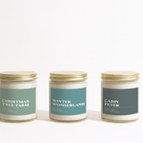 Three candles with labels 'Christmas Tree Farm', 'Winter Wonderland', and 'Cabin Fever' on a white background.