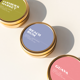 Three summer-inspired travel tin candles labeled 'Farmers Market', 'Beach Bum', and 'Guava'.